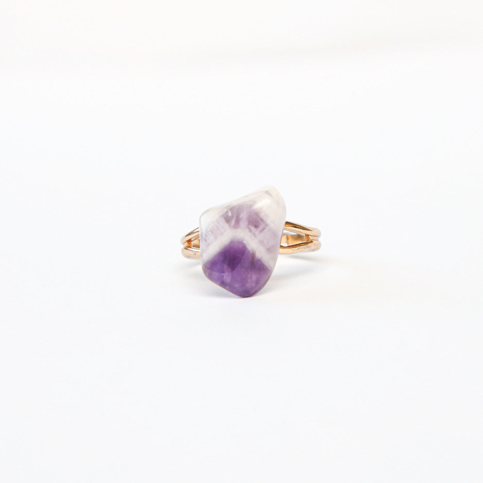 Banded amethyst stone on gold tone band ring, laying on solid white background.