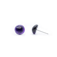 Amethyst cabochon stud earrings sitting side by side on solid white background. One sitting face forward and the other to the side showing silver tone post.