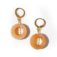 Two gold tone huggie earrings laying on solid white. They're made of orange round beads with gold bar through them, attaching to the top hoop.