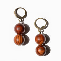 Two earrings , made of two reddish brown round wooden beads, on bronze huggie style hoops, laying on solid white background.