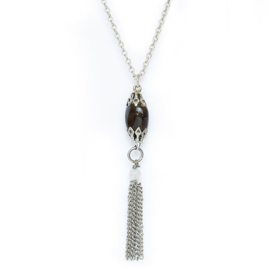 Gemstone necklace hanging on solid white background. An almost black stone, apache tear, hangs from silver attachments and chain, with an additional white beaded gemstone and chain tassel hanging below. 