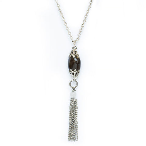 Gemstone necklace hanging on solid white background. An almost black stone, apache tear, hangs from silver attachments and chain, with an additional white beaded gemstone and chain tassel hanging below. 
