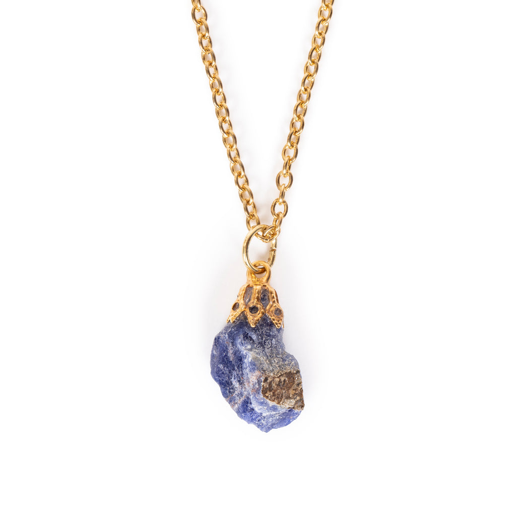 Rough cut sodalite with glue on bail, hanging on gold chain. Image has solid white background.