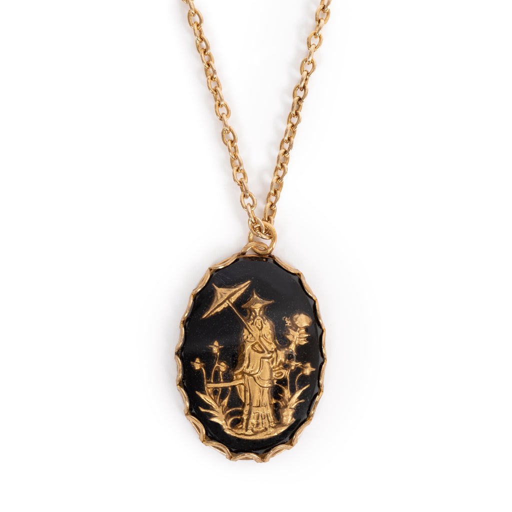 A golden traditional Japanese figure in a garden, on black back. Cab is on gold backing, hanging on gold chain. Solid white background.