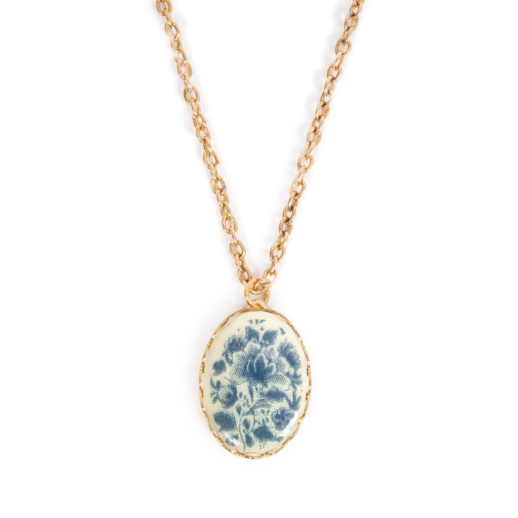 Vintage blue and cream floral design cabochon, on gold backing, hanging on gold chain. Image has a solid white background.