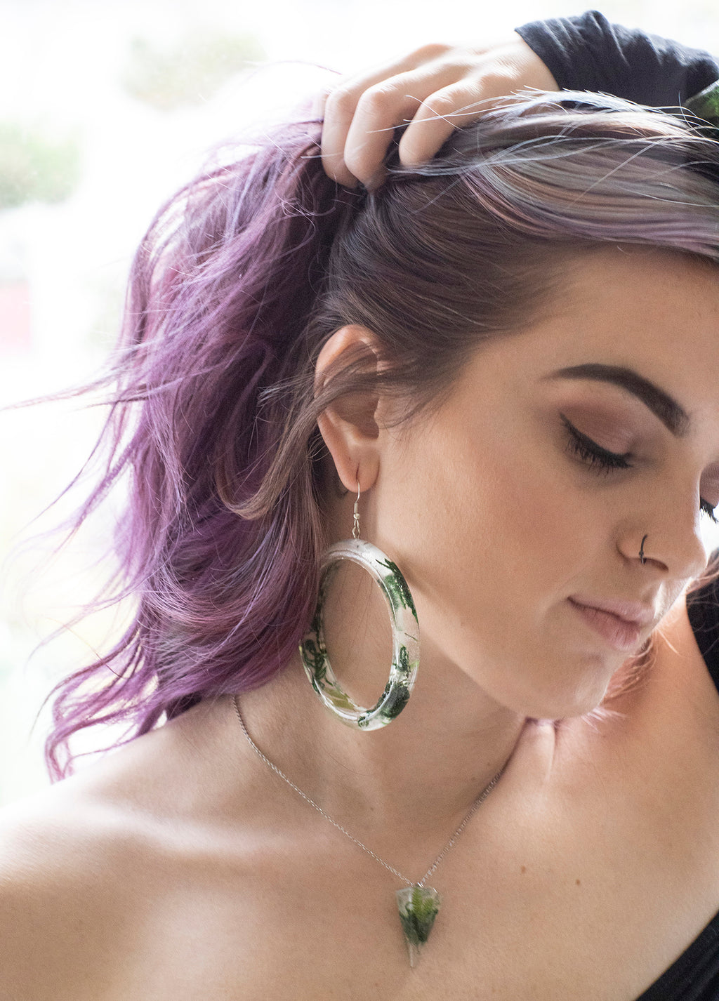 Model holding hair up, showing clear resin earrings with moss inside. 