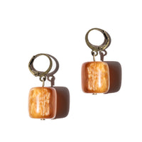 Glossy orange tone beads hang on bronze huggies. Earrings are on a solid white background. 