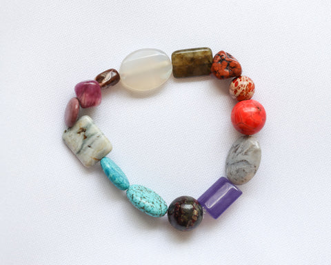 Colorful assorted gemstone bracelet, laying on lightly textured white fabric.