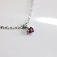 Close up of ruby on silver chain, on a white background.