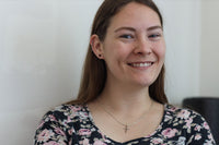 model in floral top smiling, wearing small silver cross necklace 