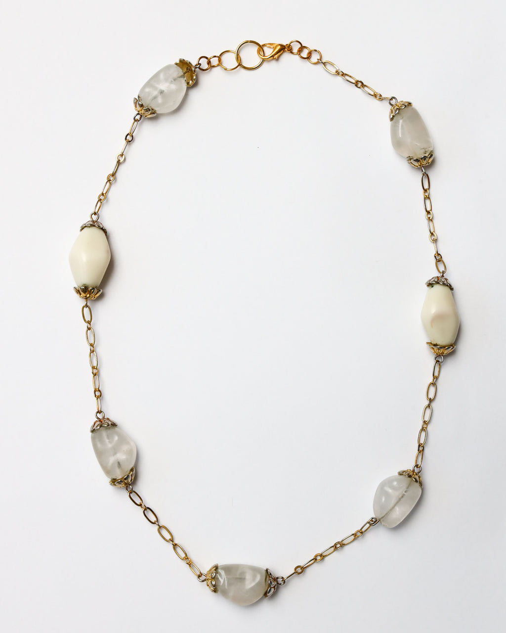 Mixed shape beads strung on gold chain. Full necklace laying on solid white background.