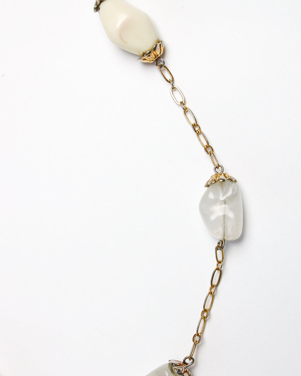 Close up detail of beaded gold strung necklace, laying on solid white background. 