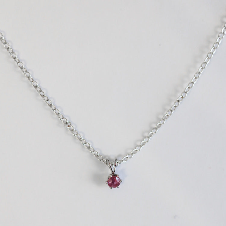 Faceted ruby hanging on silver chain, on solid white background.