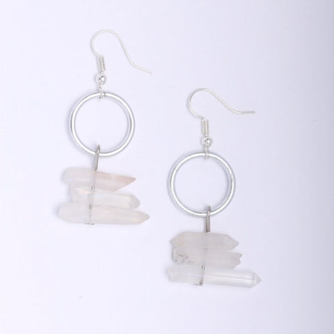 Hook style earrings, including three quartz points lay horizontally below a large metal hoop, laying on solid white background/