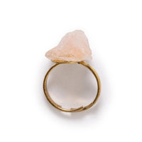 Overhead view of rough cut rose quartz ring laying on solid white background.